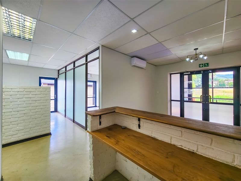 A bright, modern office space featuring a reception counter, glass partitions, suspended ceilings, and double glass entrance doors.