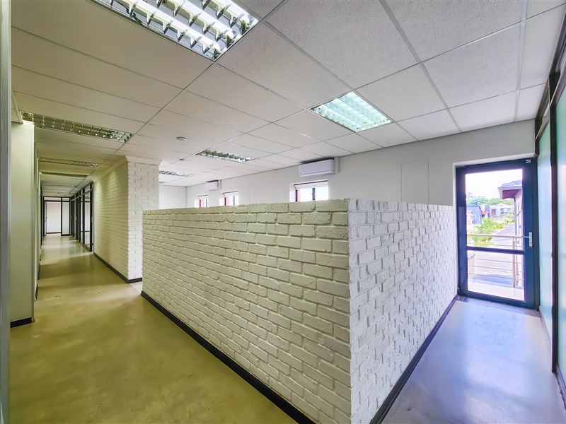 A bright, open-plan office space featuring polished concrete floors, a suspended ceiling with recessed lighting, and a distinctive white-painted exposed brick partition wall.