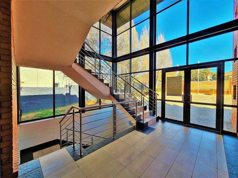 Modern office entrance lobby featuring floor-to-ceiling glass windows, a prominent staircase with stainless steel railings, and durable tiled flooring.