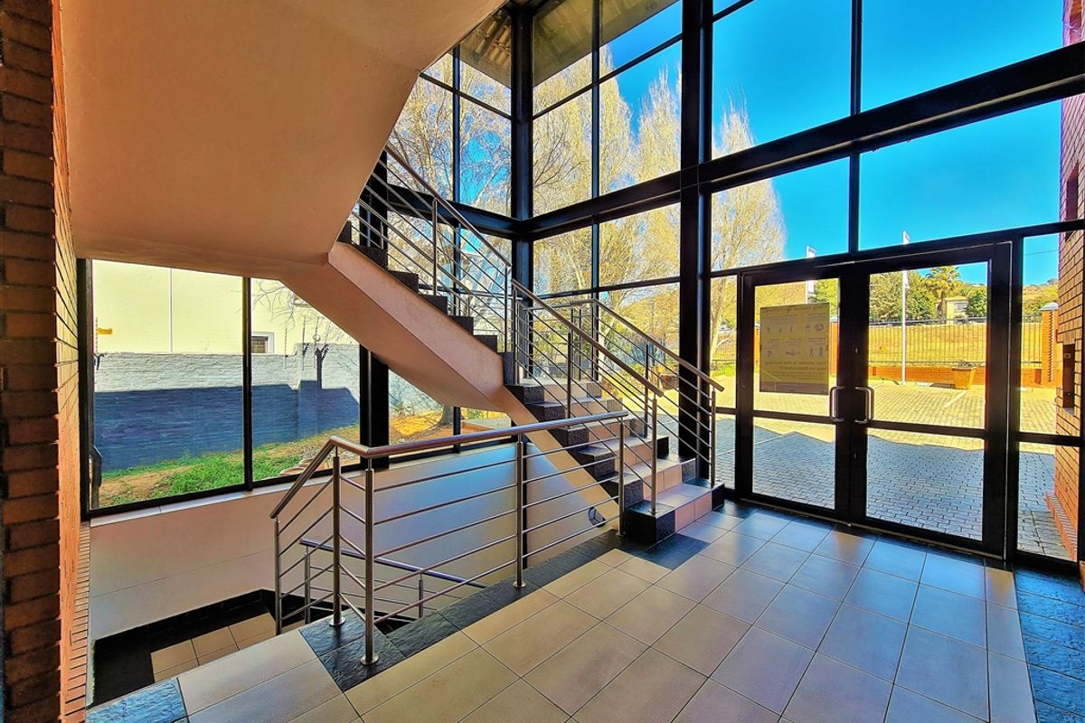 Modern office entrance lobby featuring floor-to-ceiling glass windows, a prominent staircase with stainless steel railings, and durable tiled flooring.