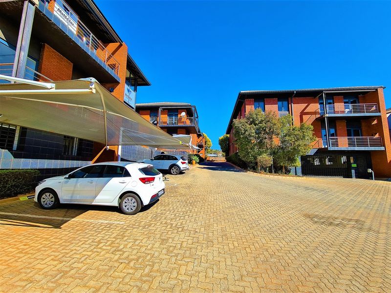 Exterior view of a modern office complex featuring brick facades, paved parking area with shade cloth carports, and multi-level balconies.