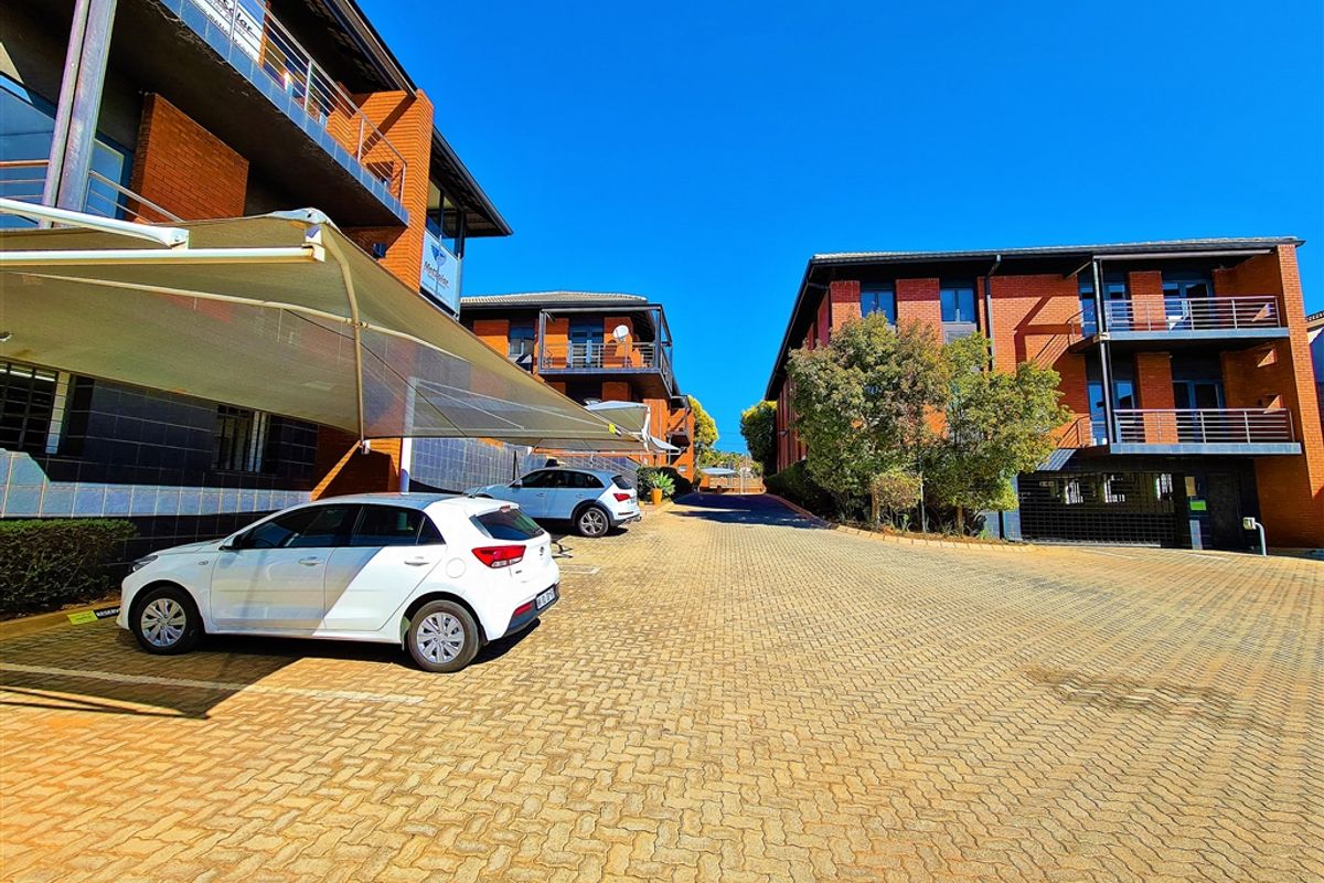 Exterior view of a modern office complex featuring brick facades, paved parking area with shade cloth carports, and multi-level balconies.
