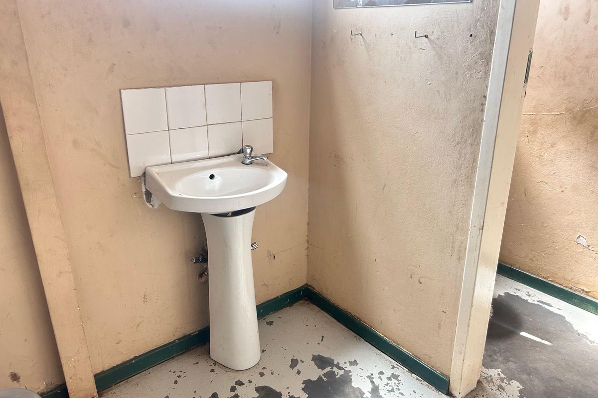 A small, dated bathroom area featuring a pedestal basin with tiled splashback, requiring significant cosmetic refurbishment and surface repairs.