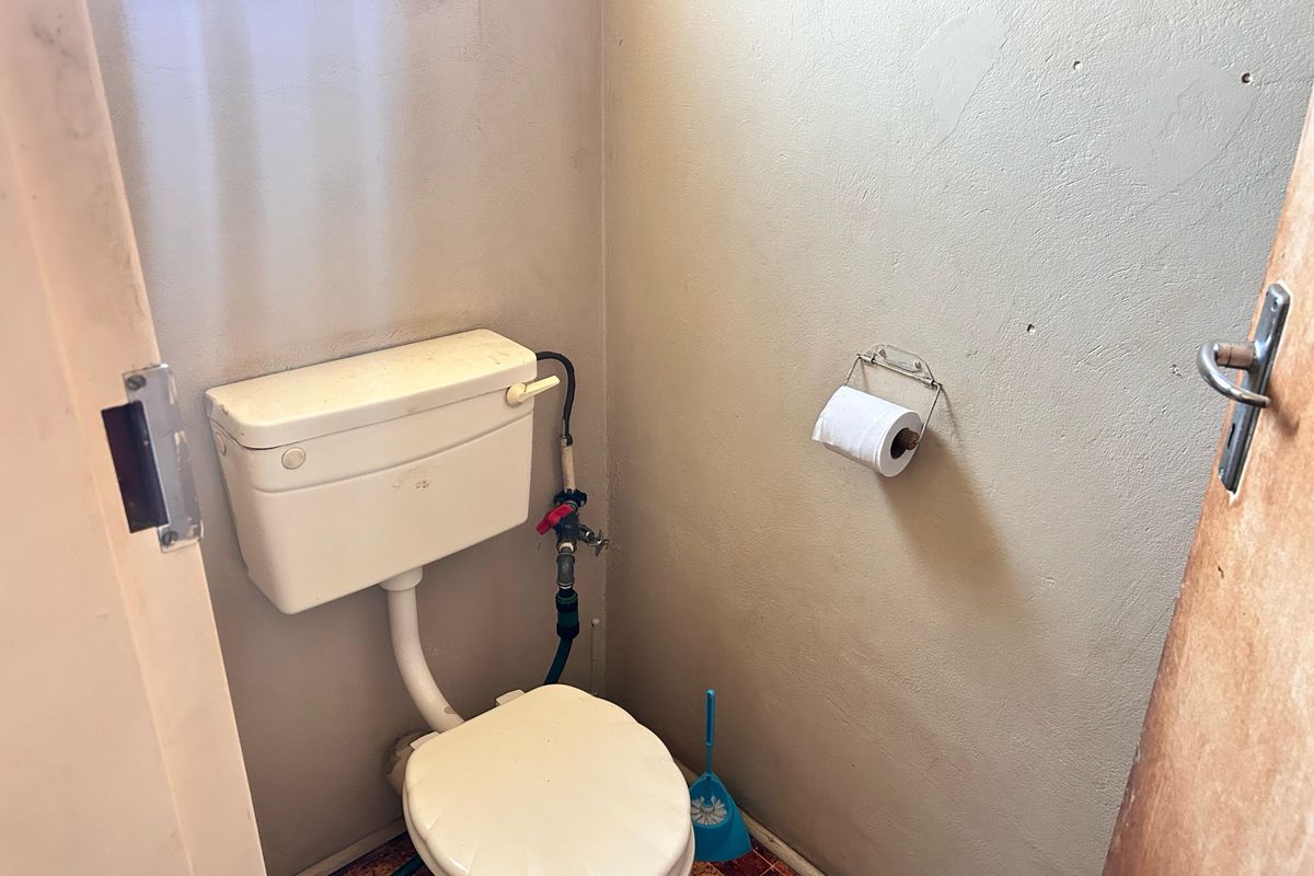 A small, dated bathroom featuring a standard toilet and basic wall finishes, requiring cosmetic updates and modernization.