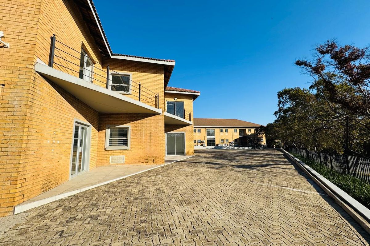 Exterior view of a multi-level office building featuring face-brick facade, paved driveway, and balcony access.