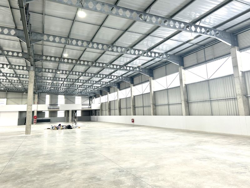 Spacious industrial warehouse featuring high ceilings with exposed steel trusses, polished concrete flooring, and a mezzanine level, suitable for various commercial or storage operations.