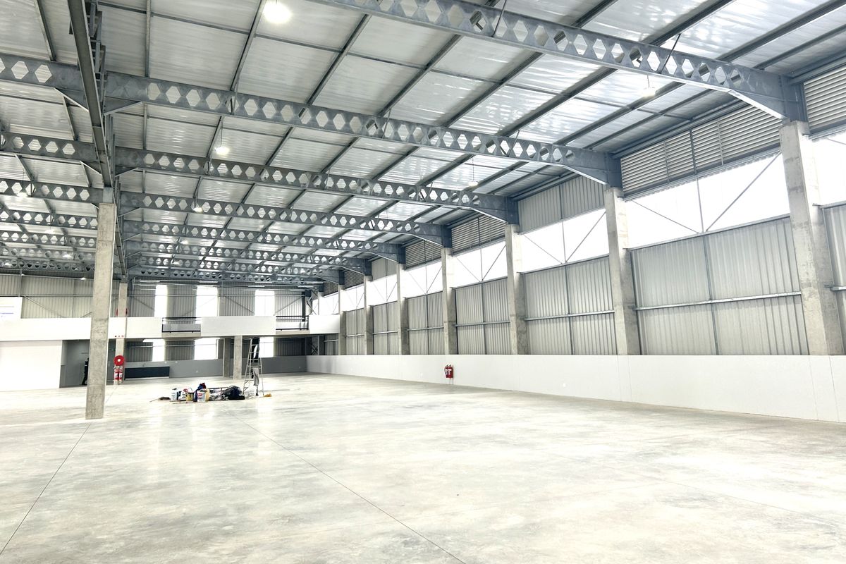 Spacious industrial warehouse featuring high ceilings with exposed steel trusses, polished concrete flooring, and a mezzanine level, suitable for various commercial or storage operations.