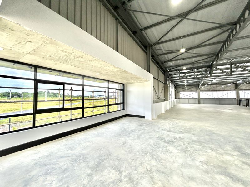 Spacious industrial open-plan area featuring high exposed steel roof trusses, polished concrete flooring, and expansive windows providing ample natural light.