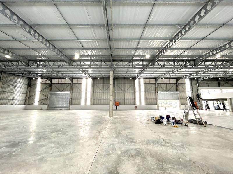 Spacious industrial warehouse featuring high-clearance steel truss roofing, polished concrete floors, and multiple roller shutter access doors.