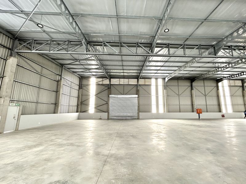 Spacious industrial warehouse featuring high ceilings with exposed steel trusses, polished concrete flooring, and a large roller shutter door for easy access.