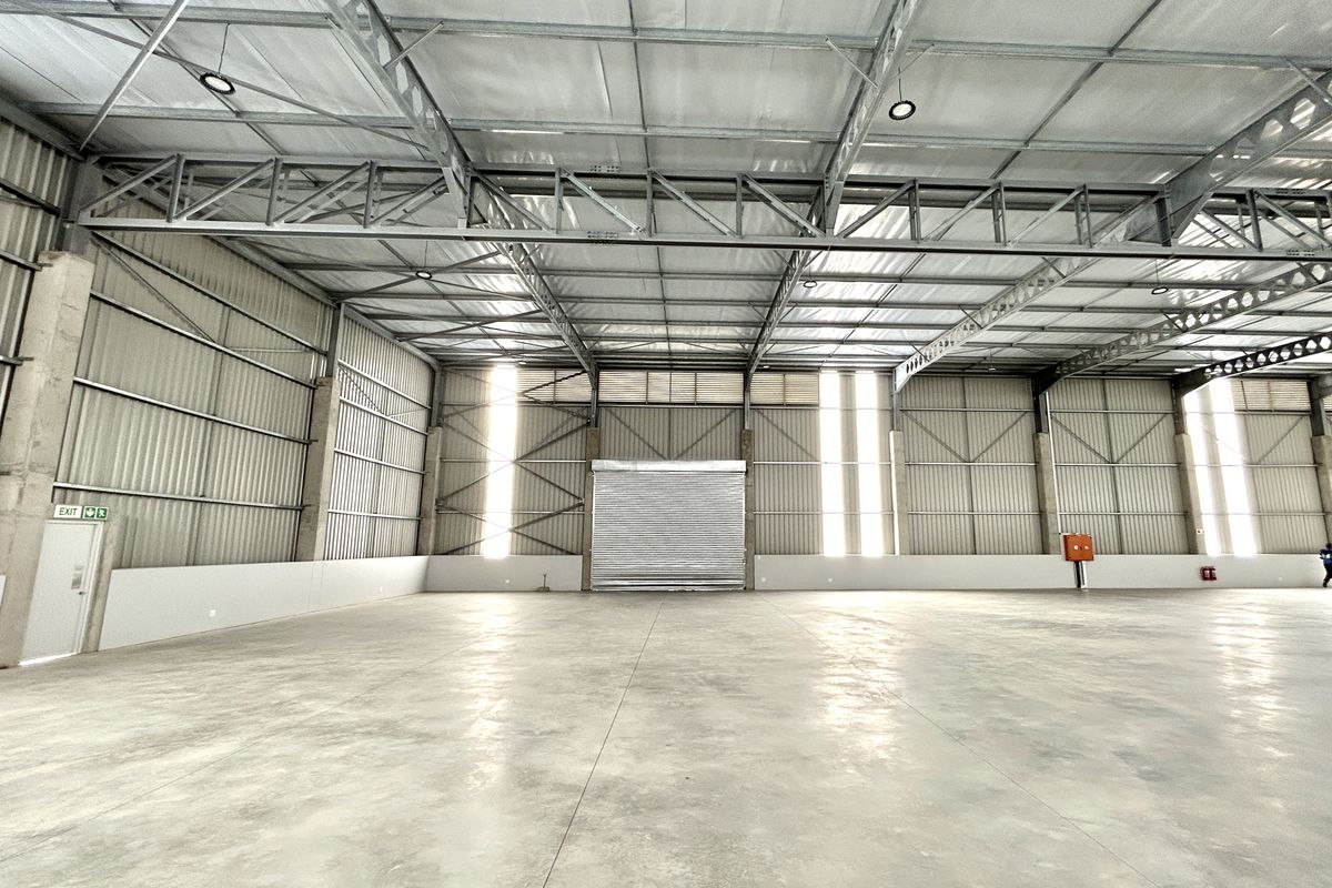 Spacious industrial warehouse featuring high ceilings with exposed steel trusses, polished concrete flooring, and a large roller shutter door for easy access.