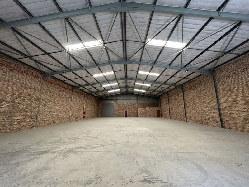 Spacious industrial warehouse featuring exposed brick walls, high-clearance steel truss roofing with integrated skylights, and durable concrete flooring.