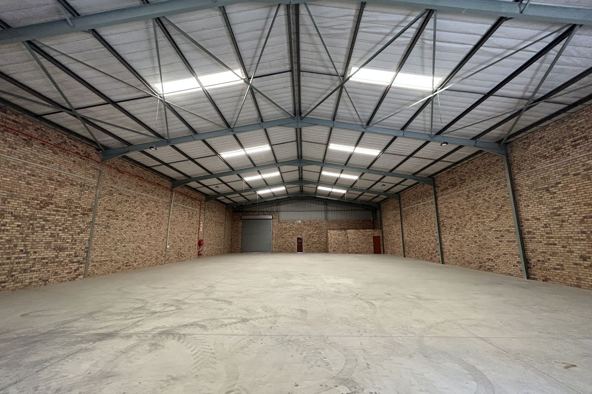 Spacious industrial warehouse featuring exposed brick walls, high-clearance steel truss roofing with integrated skylights, and durable concrete flooring.