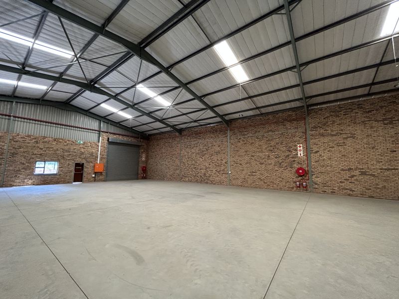 Spacious industrial warehouse unit featuring high ceilings with exposed steel trusses, concrete flooring, roller shutter access, and integrated fire safety equipment.
