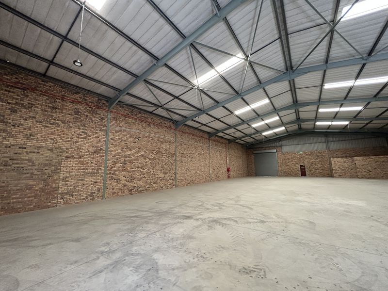 Spacious industrial warehouse featuring exposed brick walls, high-clearance steel portal frame, concrete flooring, and natural light through integrated skylights.