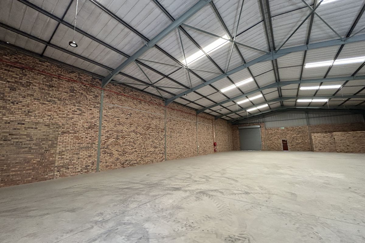 Spacious industrial warehouse featuring exposed brick walls, high-clearance steel portal frame, concrete flooring, and natural light through integrated skylights.