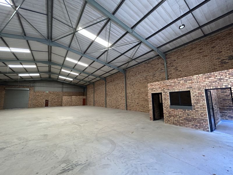 Spacious industrial warehouse featuring high-clearance steel truss roofing, durable concrete flooring, facebrick walls, and an integrated internal office structure with a roller shutter door.