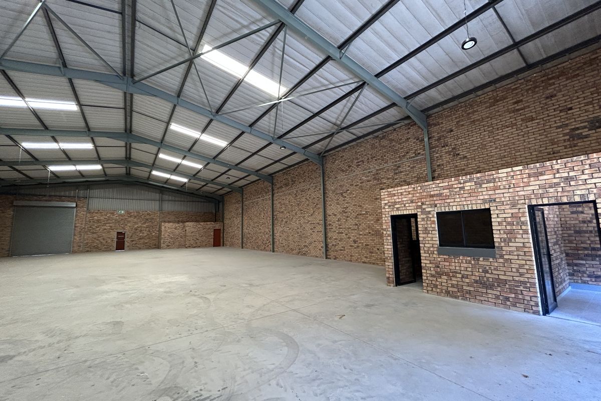 Spacious industrial warehouse featuring high-clearance steel truss roofing, durable concrete flooring, facebrick walls, and an integrated internal office structure with a roller shutter door.