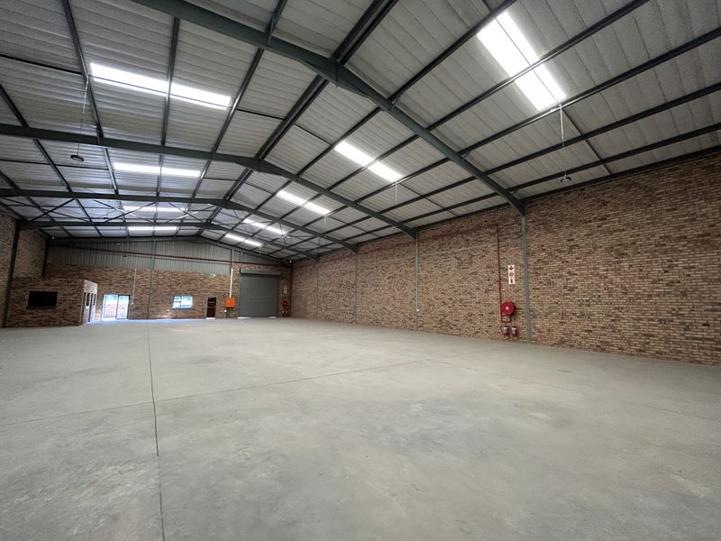 Spacious industrial warehouse featuring exposed brick walls, concrete flooring, high steel truss ceilings with integrated skylights, and essential fire safety equipment.