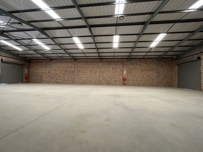 Spacious industrial warehouse featuring high ceilings with skylights, concrete flooring, exposed brick walls, and two large roller shutter doors for easy access.