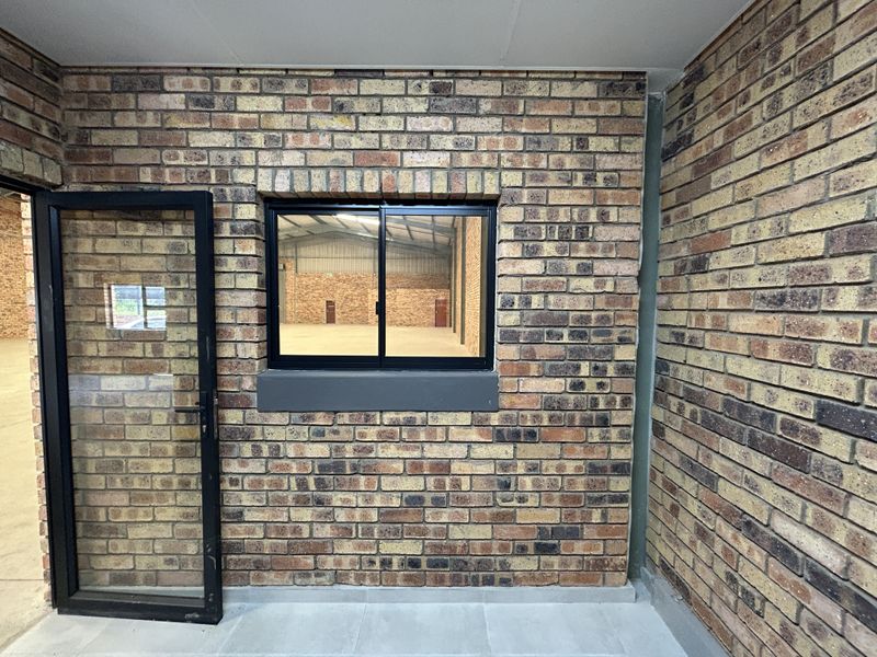 A clean, modern industrial entry area featuring exposed brick walls, tiled flooring, and an aluminium-framed glass door looking into the warehouse space.