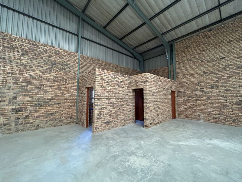 Spacious industrial warehouse unit featuring exposed brick walls, high-clearance steel portal frame construction, and durable concrete flooring with internal partitioned utility rooms.