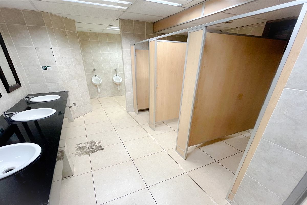 A functional office restroom featuring multiple stalls, wall-mounted urinals, and a long vanity with three integrated sinks.