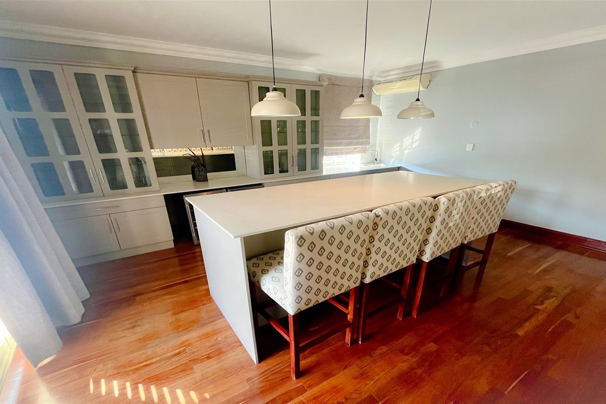 A well-appointed office kitchenette featuring custom cabinetry, a central island with seating, and polished hardwood flooring.