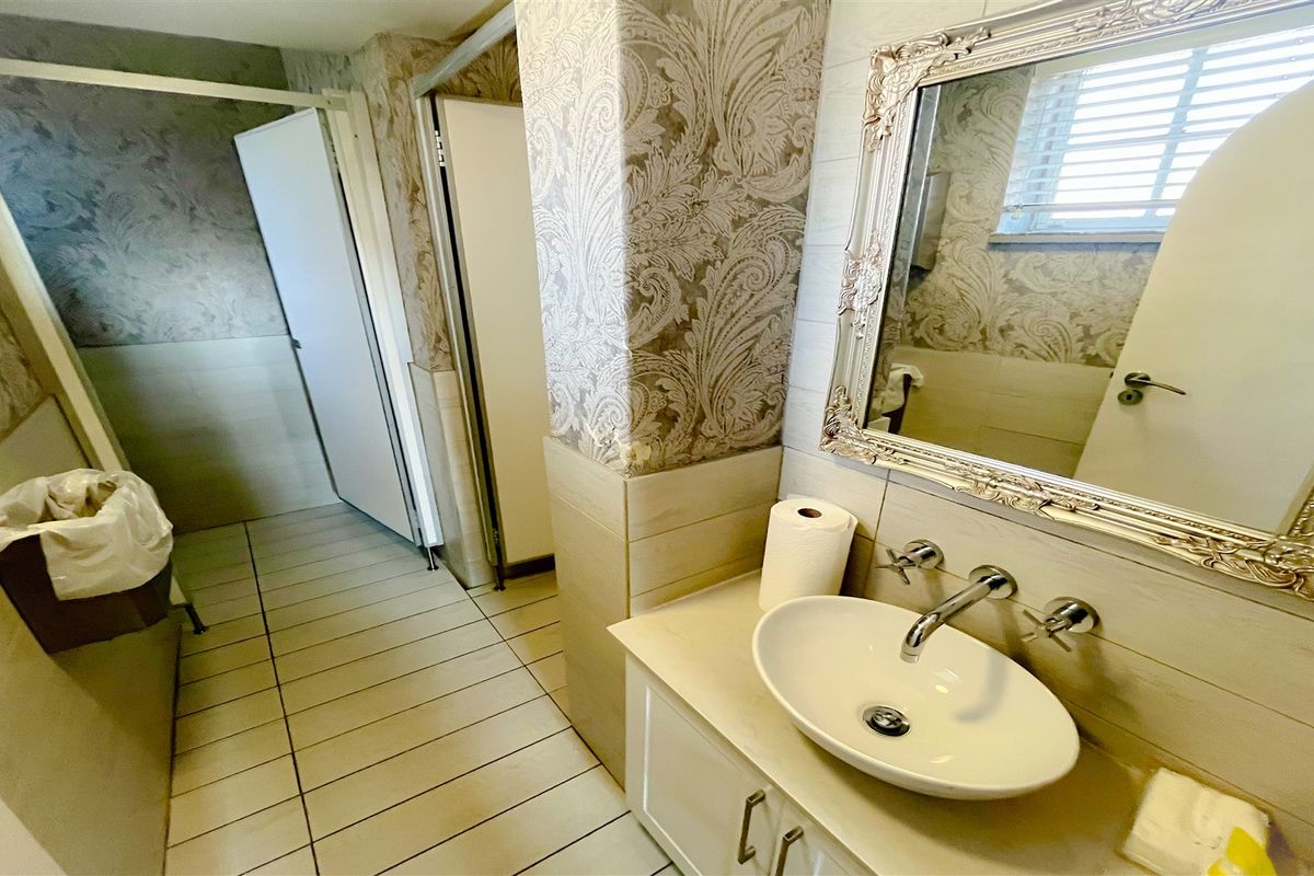 A functional office bathroom featuring a modern vessel sink, wall-mounted chrome faucet, vanity cabinetry, and decorative patterned wallpaper.