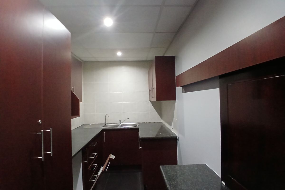 A functional office kitchenette featuring dark wood cabinetry, granite countertops, a stainless steel double sink, and recessed ceiling lighting.