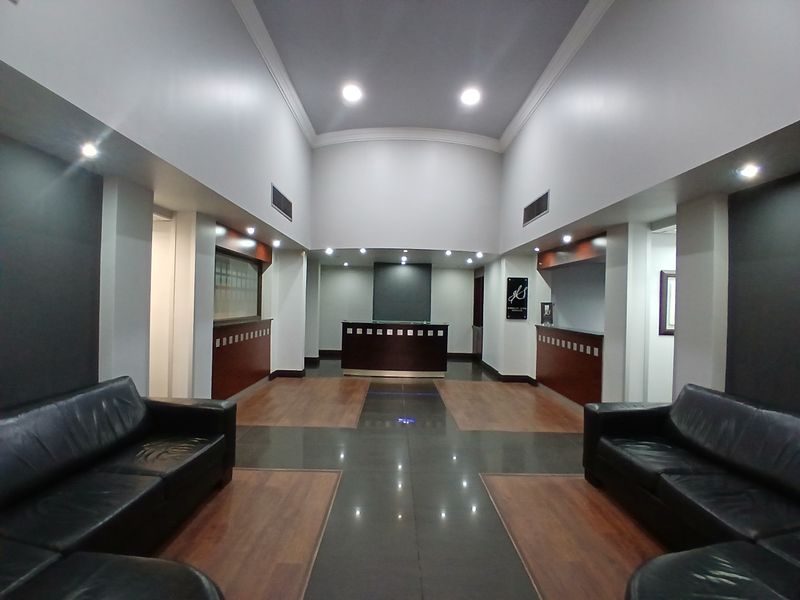 A professional office reception area featuring a central reception desk, high ceilings with recessed lighting, and a combination of laminate and tiled flooring.