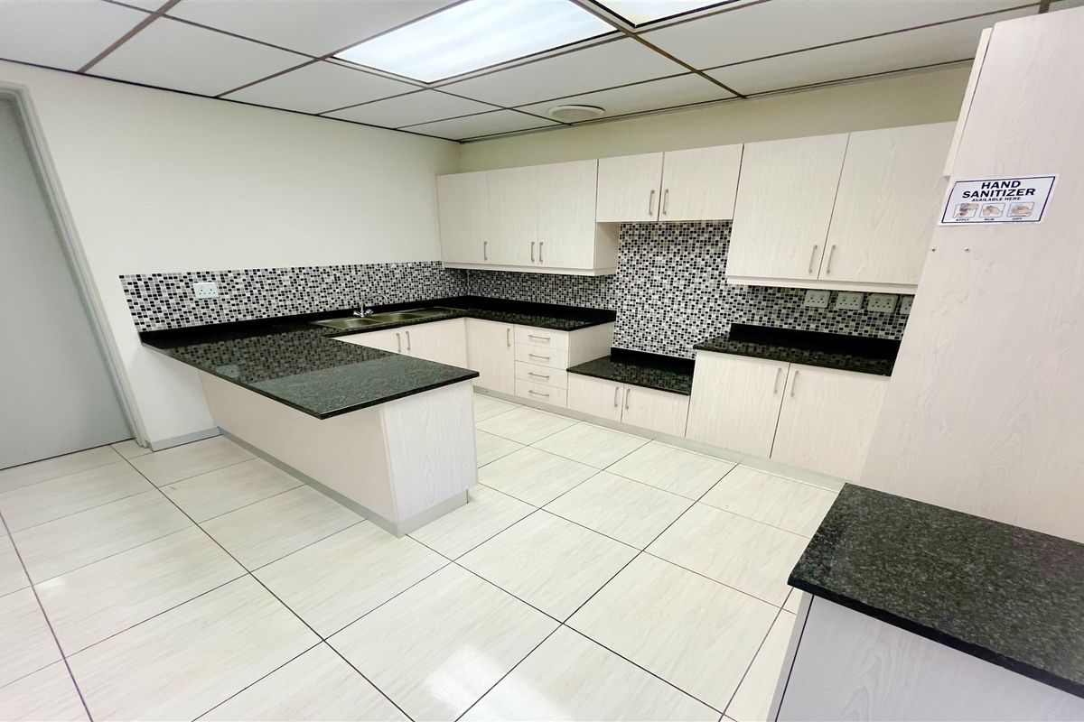 A clean office kitchenette featuring light wood-grain cabinetry, dark granite countertops, mosaic tile backsplash, and white tiled flooring with a drop ceiling.