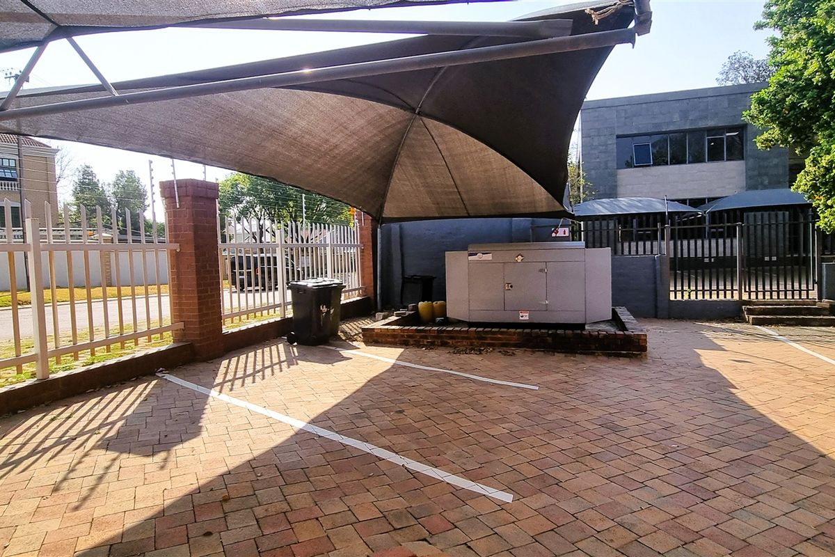 Outdoor parking area featuring paved surfacing, a shade cloth canopy, and a dedicated generator enclosure within a secure office property perimeter.