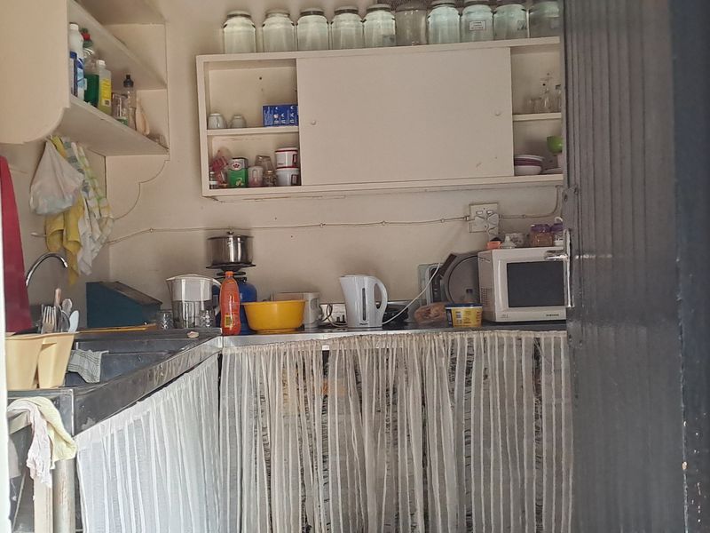 A compact scullery or prep area featuring stainless steel sink, wall-mounted cabinetry, and open shelving, providing functional utility space.