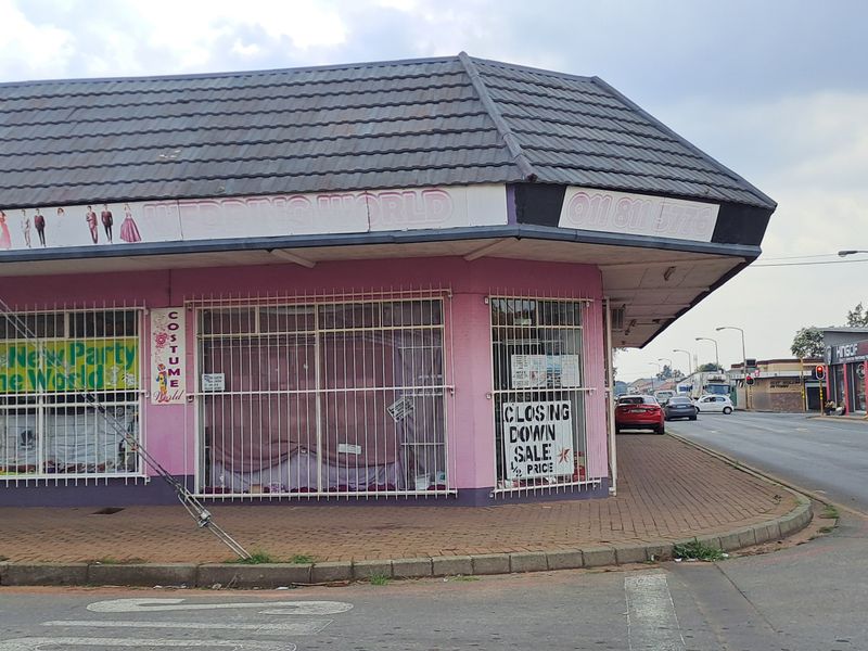 Corner commercial property featuring large display windows, security bars, and a tiled roof, situated on a street-facing lot.