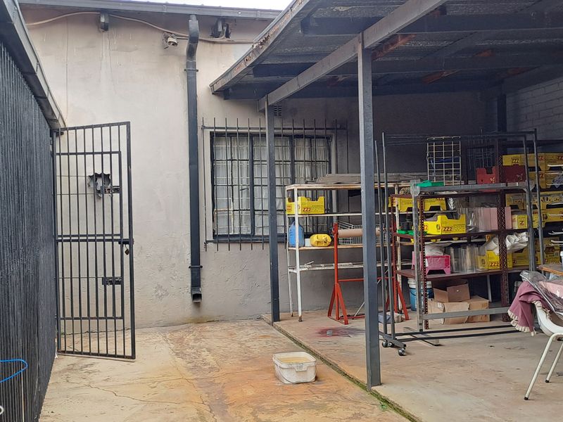 A covered outdoor utility area featuring concrete flooring, security gates, and metal roofing, currently used for storage.