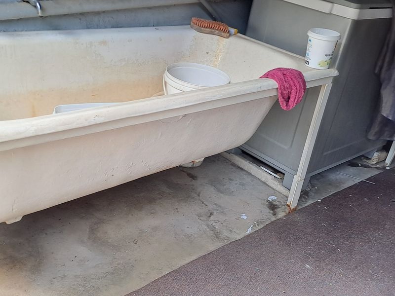 A utility or laundry area featuring a heavily stained freestanding bathtub and exposed plumbing connections on a concrete floor.