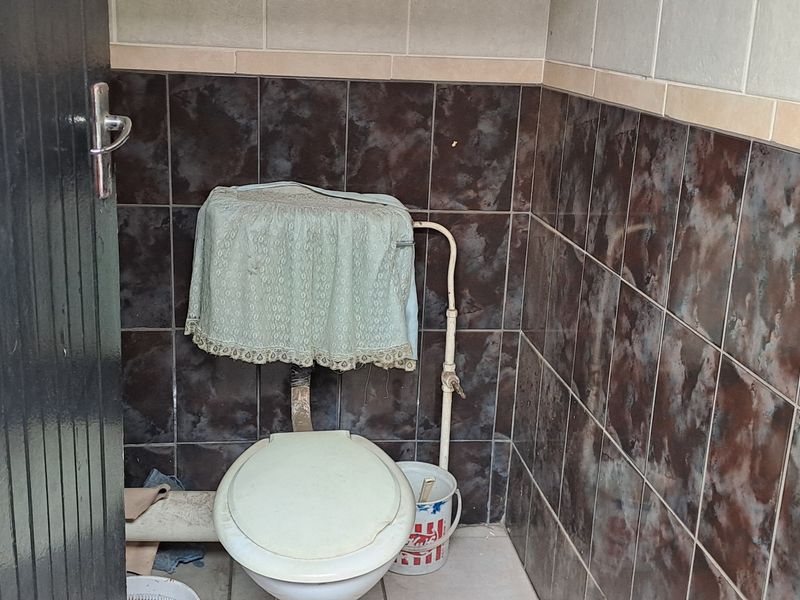 A small, dated bathroom featuring tiled walls and a standard toilet fixture, requiring modernization and cosmetic updates.