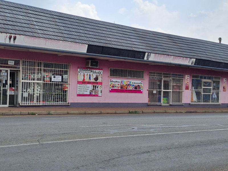 Street-facing commercial storefront featuring a tiled roof, large glass display windows with security bars, and prominent signage.