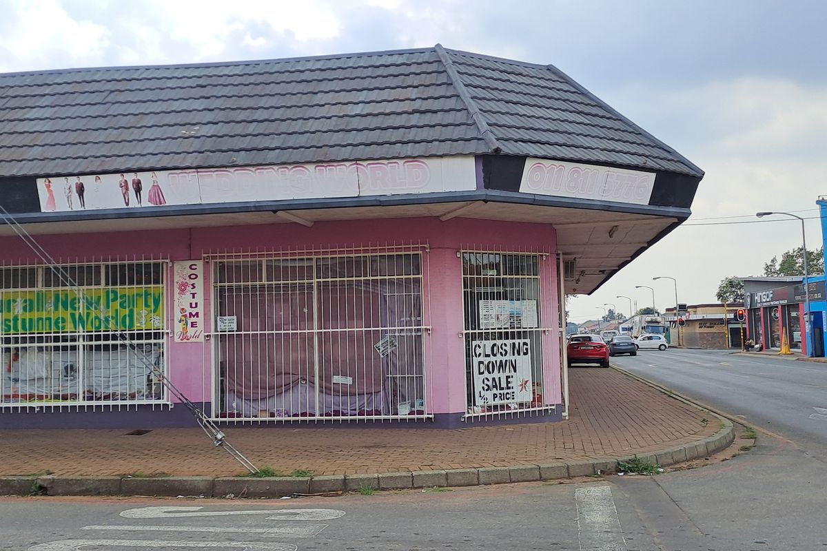 Corner commercial property featuring large display windows, security bars, and a tiled roof, situated on a street-facing lot.