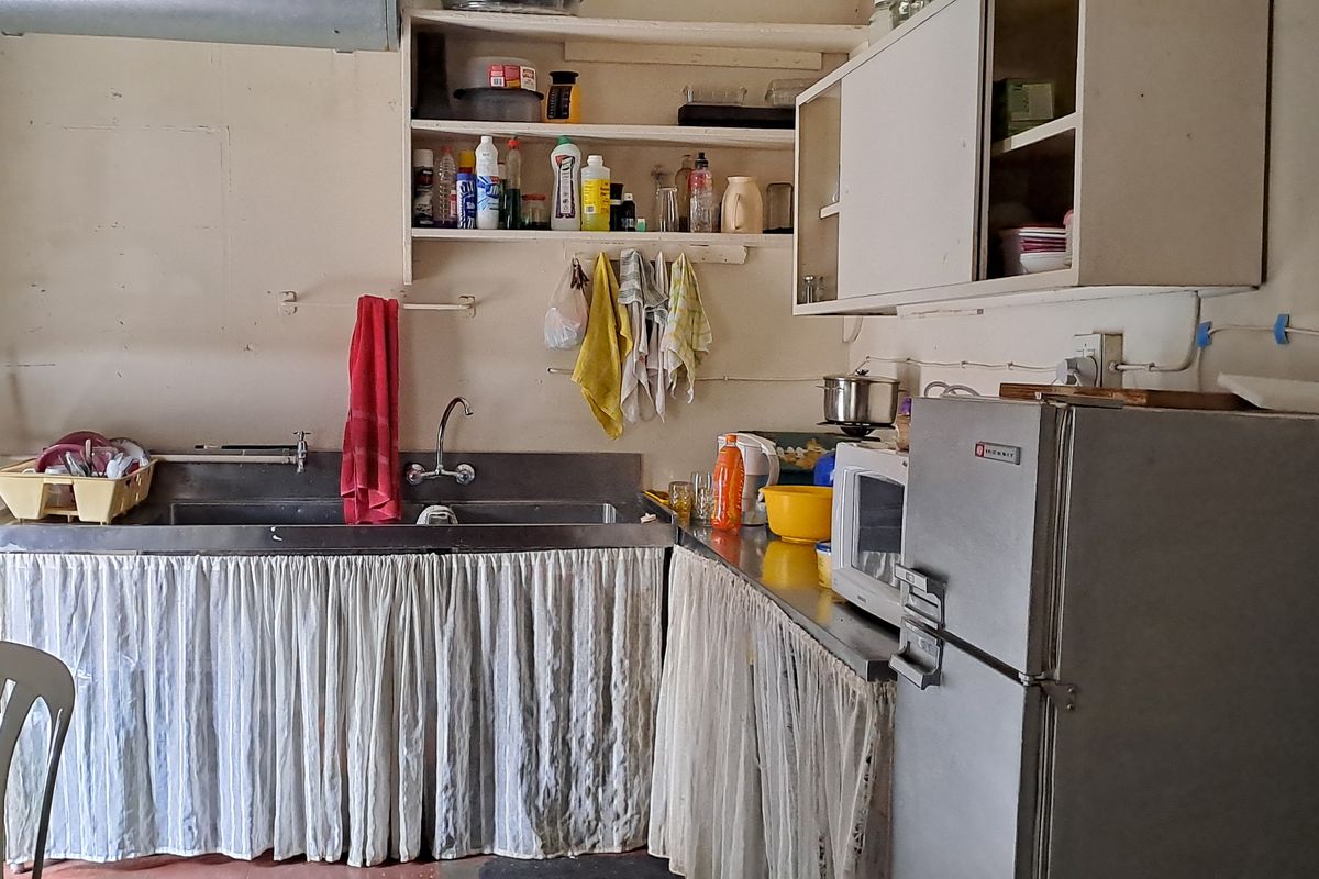 A dated kitchen area featuring a stainless steel sink, open shelving, and basic cabinetry, requiring modernization and renovation to improve functionality and aesthetic appeal.