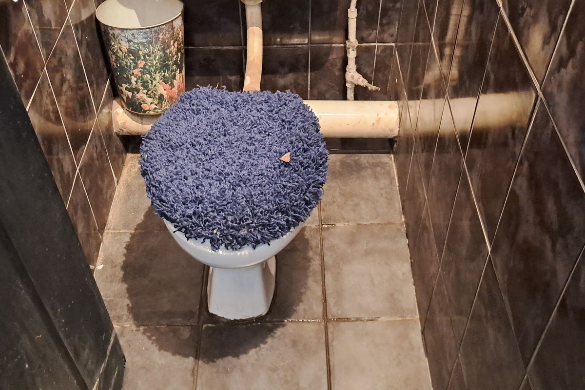A small bathroom featuring dark ceramic wall and floor tiles with an exposed plumbing configuration.