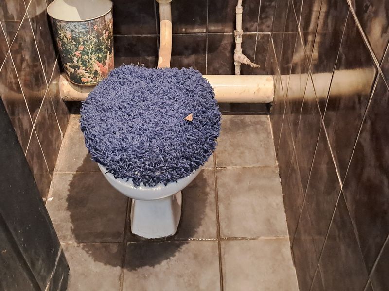 A small bathroom featuring dark ceramic wall and floor tiles with an exposed plumbing configuration.