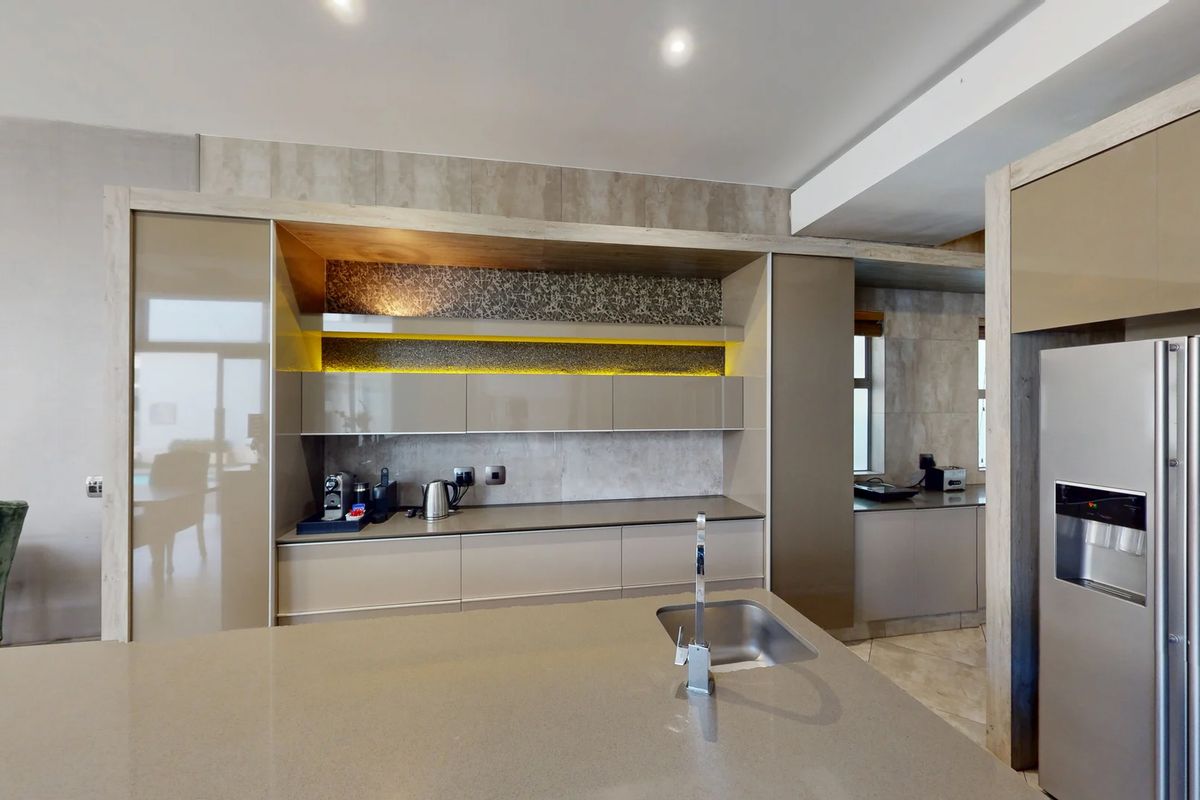 Modern kitchen featuring sleek built-in cabinetry, stone countertops, a central island with an undermount sink, and integrated accent lighting.