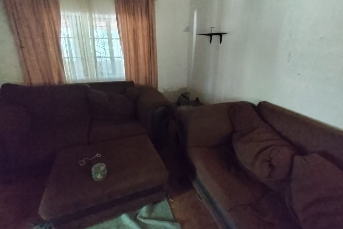 A living room area featuring tiled flooring and window treatments, currently requiring cosmetic updates and wall repairs to improve the overall aesthetic.