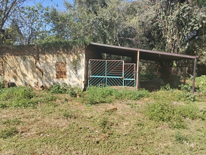 A dilapidated utility structure featuring brick masonry walls with significant structural cracking and a metal gate, situated in an overgrown outdoor area.