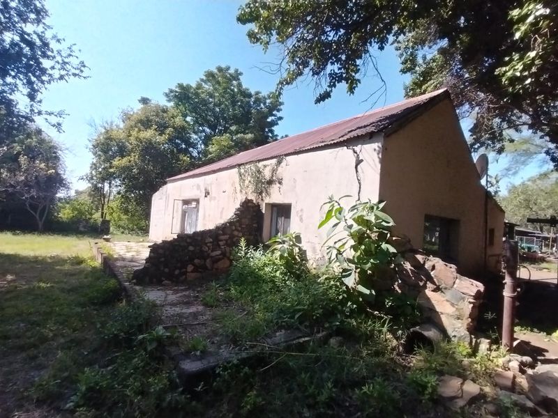 Rear view of a rustic farm building featuring stone and plastered walls with a corrugated metal roof, showing significant signs of weathering and structural wear.