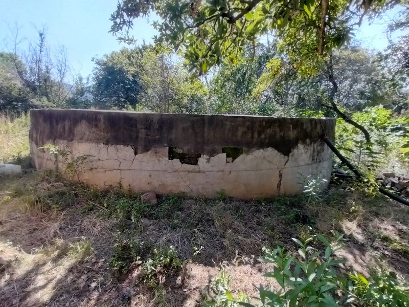 A circular concrete water reservoir located on the farm grounds, showing significant signs of structural wear and surface deterioration.