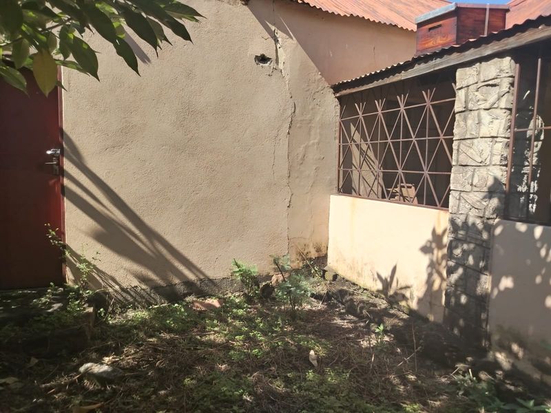 Rear exterior view of the farm building showing a plastered wall with significant structural cracking and a metal security gate.