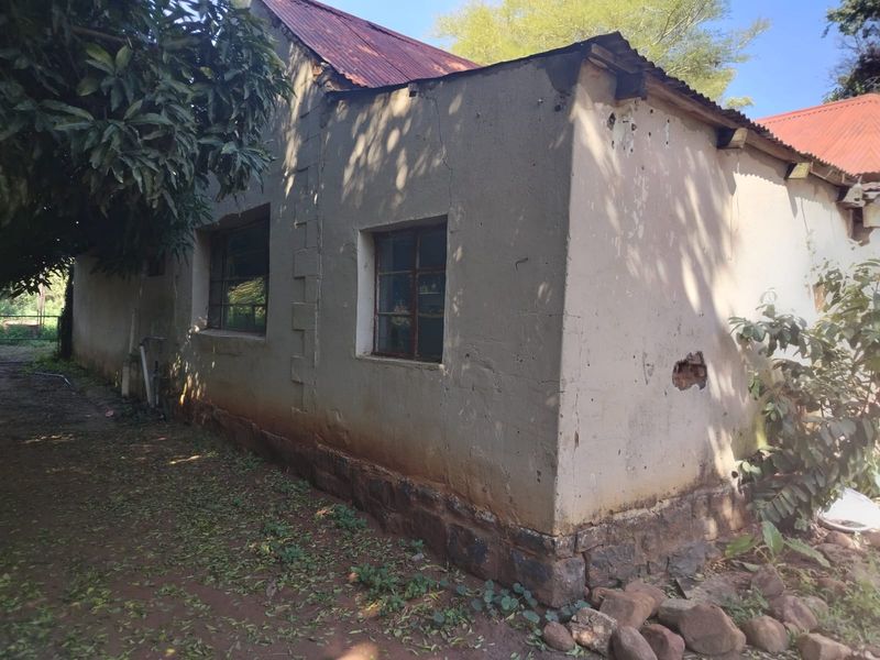 Exterior view of a farm building showing a corrugated metal roof, stone foundation, and visible wear to the plaster and window frames.